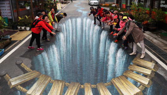 26일 오후 경기도 양평군 용문산관광지를 찾은 관광객들이 바닥에 그려진 트릭아트를 보며 즐거워하고 있다. 양평군은 청춘뮤지엄(트릭아이뮤지엄)과 양평군귀농귀촌협동조합의 재능 기부로 용문산관광지 반경 1㎞ 구역에 길이 120m, 폭 8m 크기의 대형 물길 그림을 비롯한 50여점의 착시그림을 선보일 예정이다.